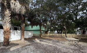Ein umzäunter Garten mit Kiesweg, einer Holzbank und einer kleinen Feuerstelle.