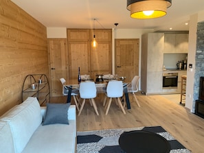 Ein modernes Wohnzimmer mit einer Couch, einem Esstisch, Stühlen, Holzwänden, einer Küchenzeile und einem Kamin aus Stein.