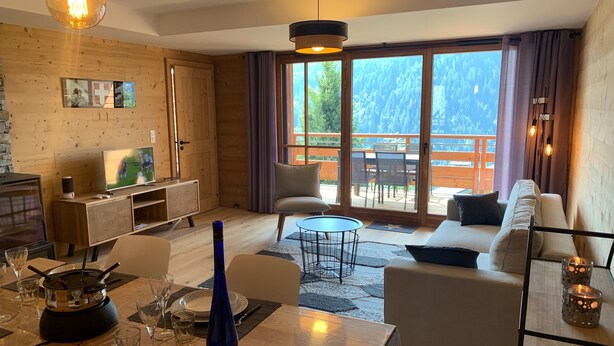 Un salon moderne avec un plancher en bois, un canapé, une table à manger dressée avec des assiettes et des verres, un téléviseur et une cheminée.