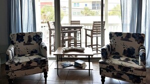 Ein Zimmer mit zwei Sesseln, einem kleinen Tisch und Blick durch eine Glastür auf einen Außenbereich mit Tisch und Stühlen.