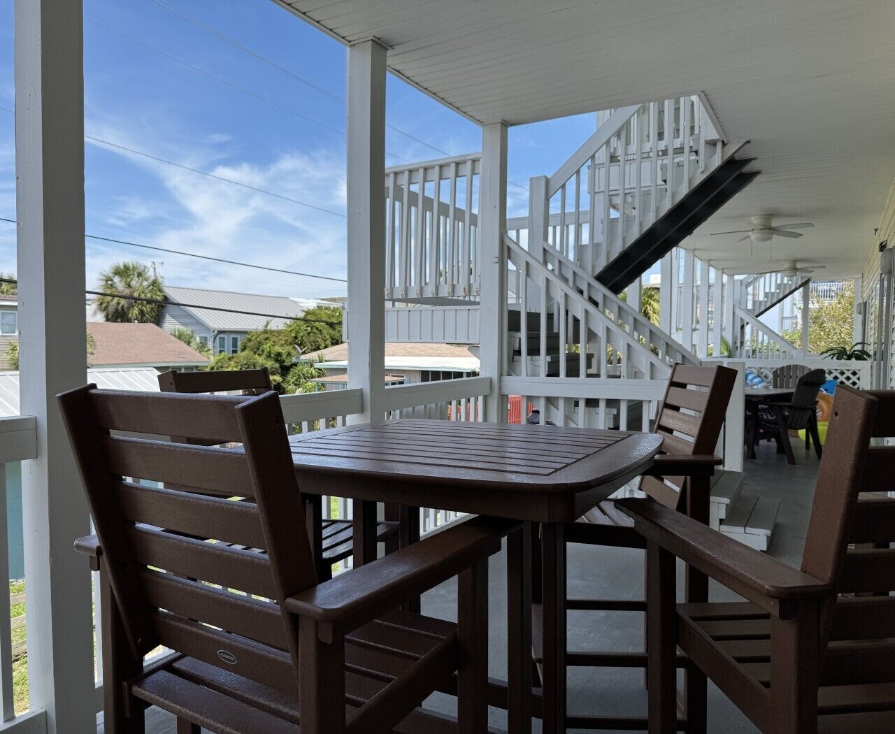 A covered outdoor area with a table and chairs, a staircase, and a view of the neighborhood.