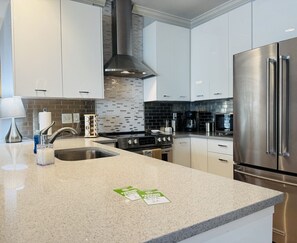 Une cuisine moderne dotée d’appareils électroménagers en acier inoxydable, d’un plan de travail en granit et de meubles de rangement blancs.