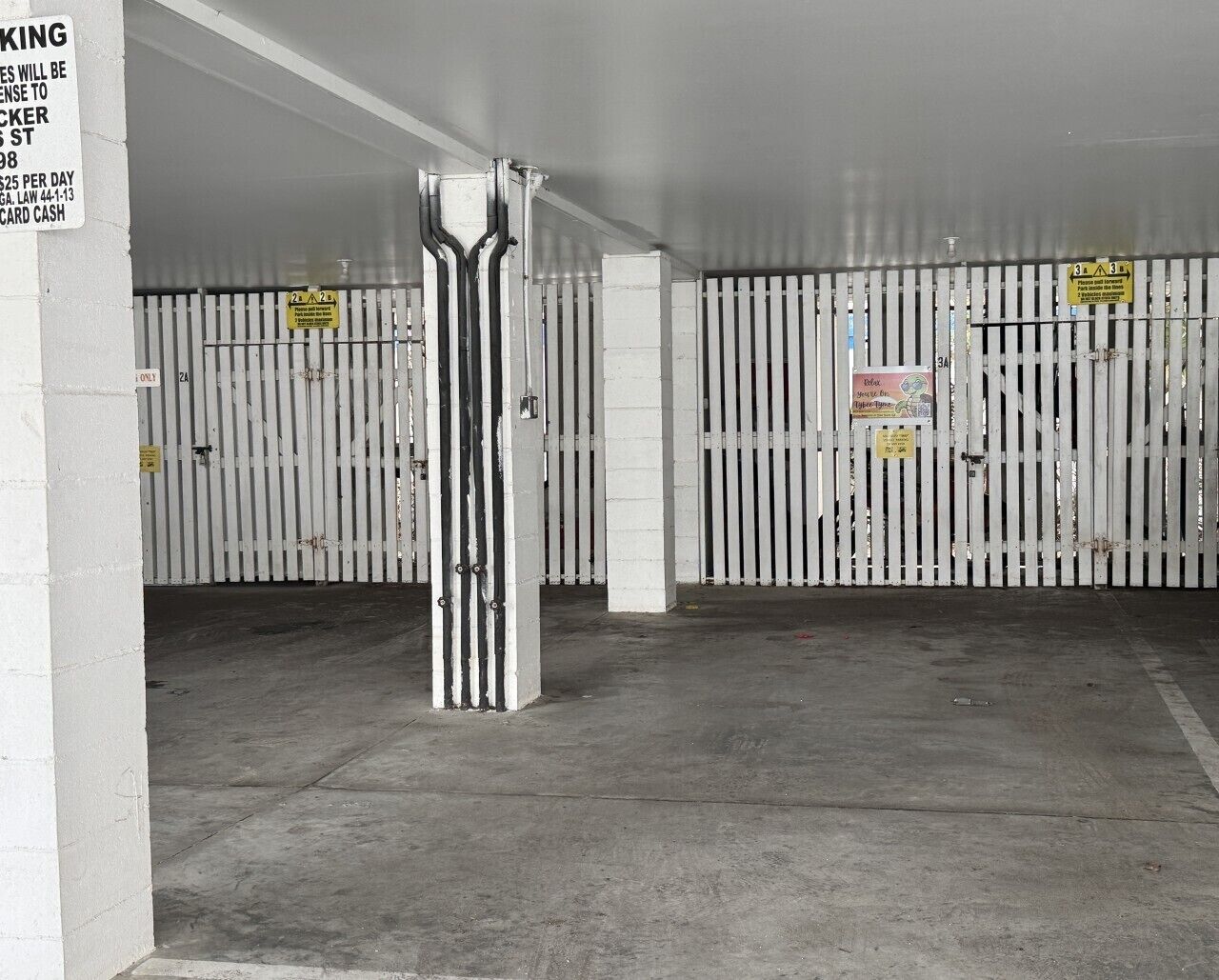 A parking garage with white metal gates, concrete pillars, and a sign indicating a $25 daily parking fee.
