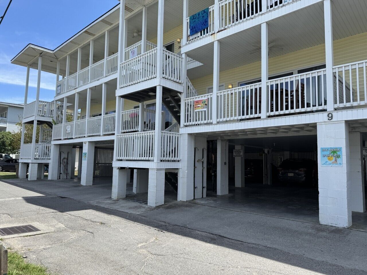 A multi-story building with balconies, a covered parking area, and a sign indicating a beach location.