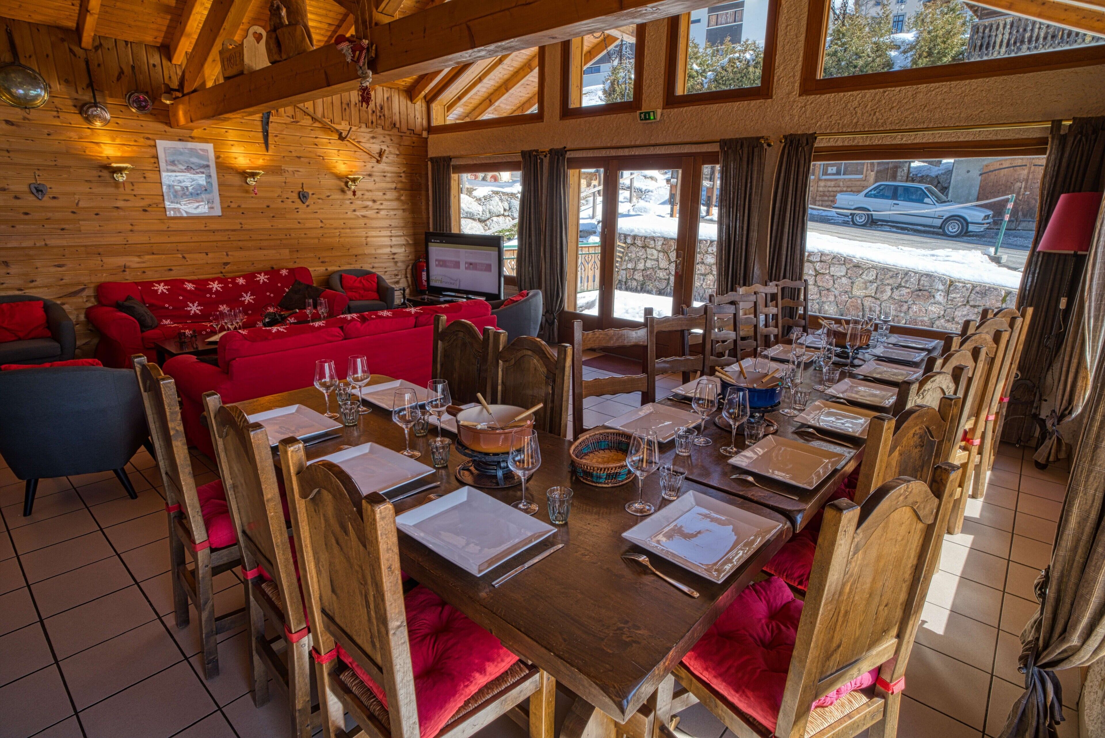 A wooden interior with a dining table set for six, red upholstered seating, and a television in the background.