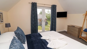 A bedroom with a bed, a dresser, a TV, and a balcony with curtains. - Lodge 21 - Bluebell (Brigg)