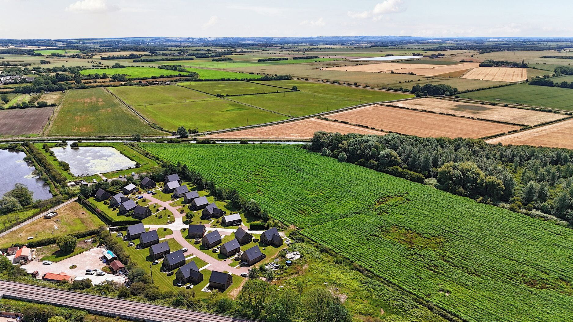 A rural landscape with fields, a small cluster of houses, and a railway track.