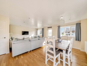 Un salon moderne comprenant un canapé, une table à manger avec des chaises, un téléviseur à écran plat fixé au mur et une fenêtre avec des rideaux.