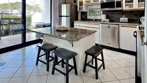 A modern kitchen with a large island, stainless steel appliances, and a view of the outdoors. - Maui Parkshore 116 (Kihei)
