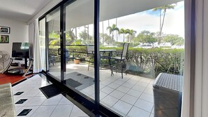 A modern living room with a large sliding glass door leading to a balcony with outdoor furniture. - Maui Parkshore 116 (Kihei)