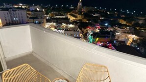 Un balcón con dos sillas de mimbre y una mesita redonda, con vista a un paisaje urbano nocturno.