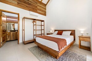 A bedroom with a wooden bed, a nightstand, a wardrobe, and a bathroom with a mirror and sink. - Boutique Villa 5 Suites with Private Pool in Playa Avellanas. 5 min from the sea (Guanacaste Province)