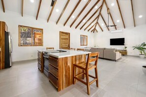 A spacious kitchen with a central island, wooden ceiling beams, and a large window. - Boutique Villa 5 Suites with Private Pool in Playa Avellanas. 5 min from the sea (Guanacaste Province)