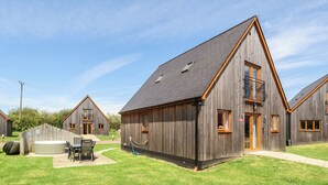 A row of wooden cabins with a patio area and a small table with chairs. - Lodge 23 - Priscilla (Brigg)