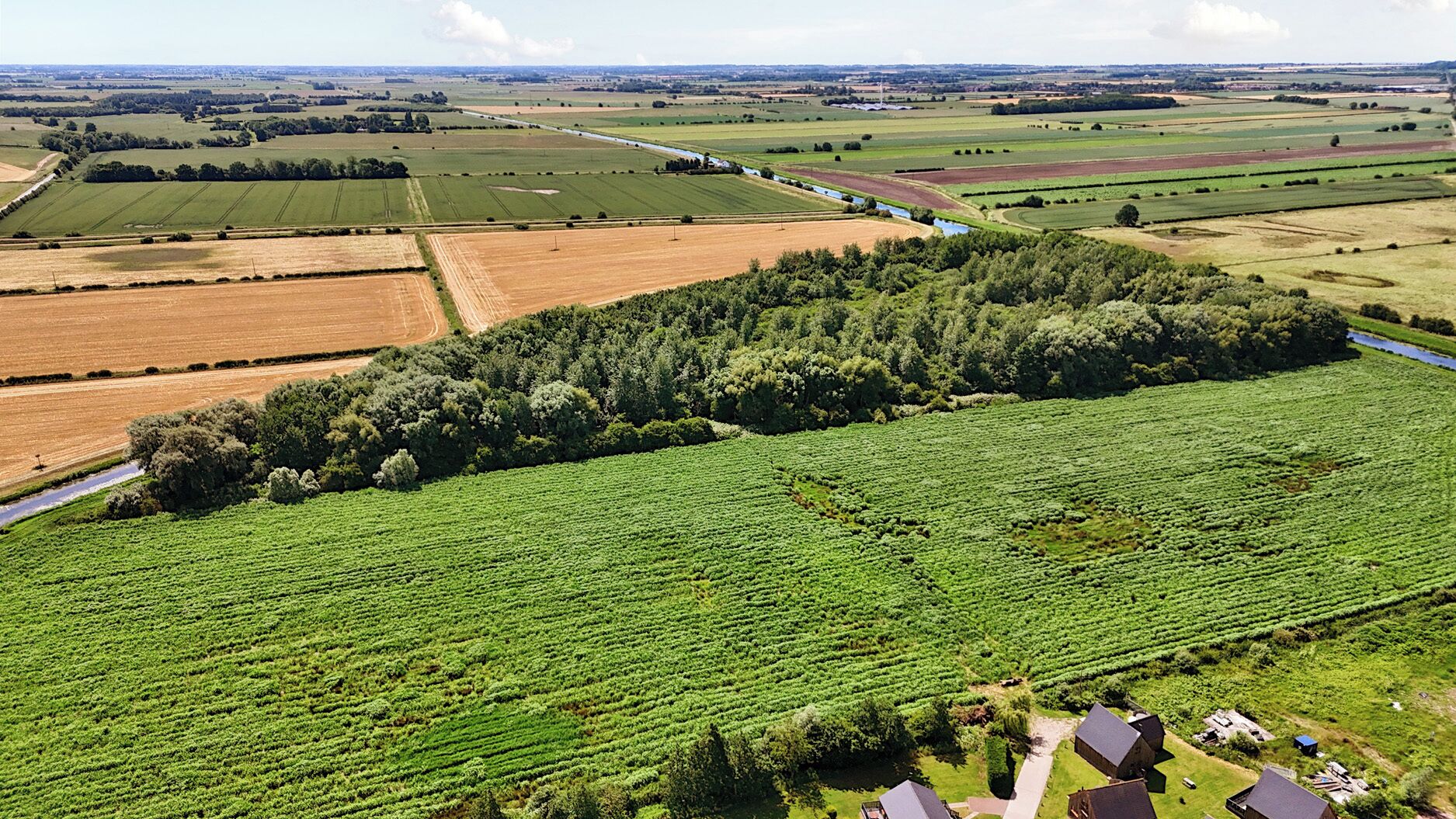 Une vue aérienne d’un paysage rural, avec des champs, une rivière et quelques bâtiments dispersés.