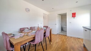 A dining area with a wooden table, pink chairs, and a clock on the wall. - Lodge 23 - Priscilla (Brigg)