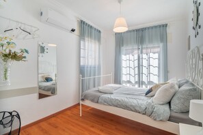 Een slaapkamer met een bed, nachtkastje, spiegel en een raam met gordijnen.