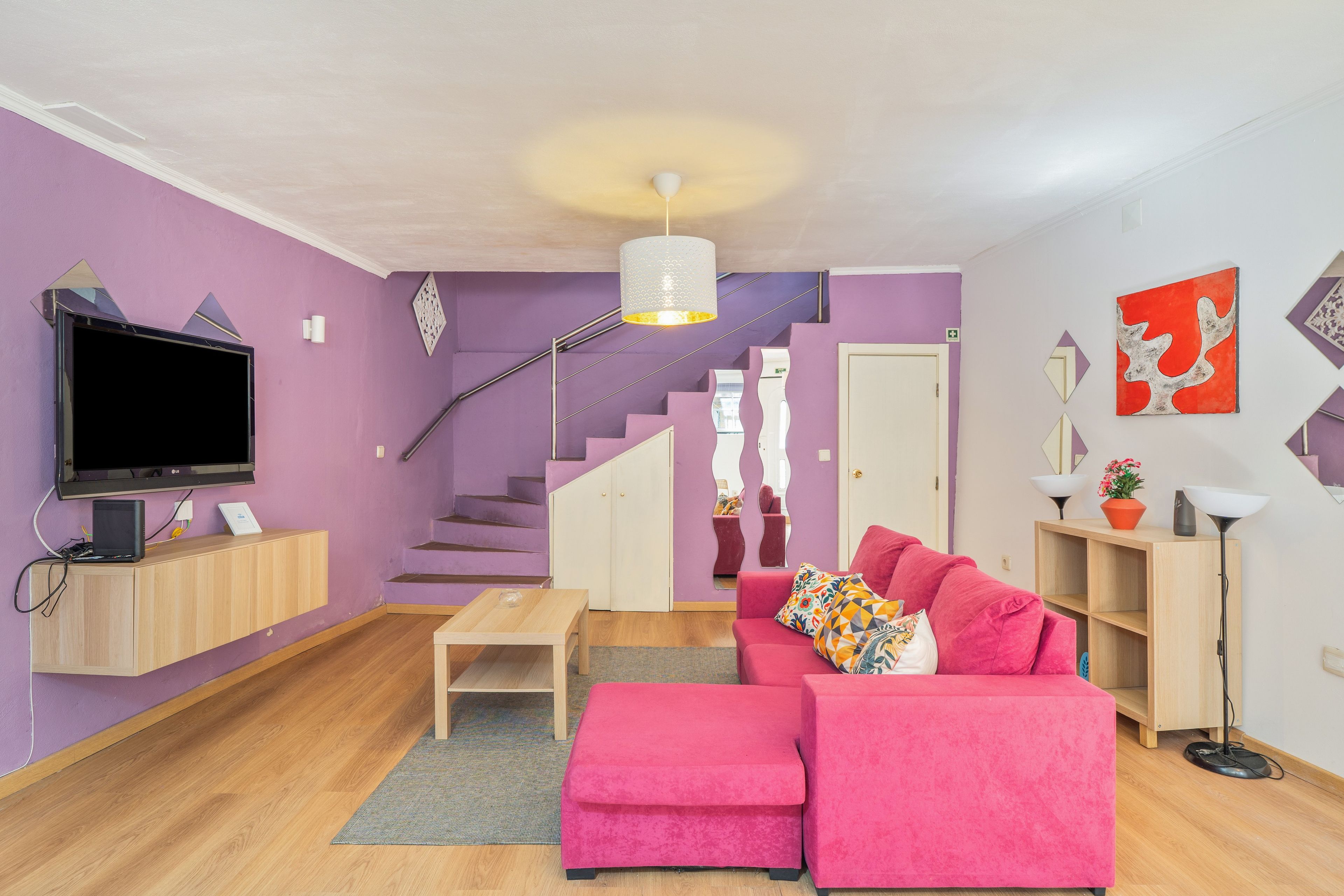 Ein modernes Wohnzimmer mit einem rosafarbenen Sofa, einem Flachbildfernseher und einer Treppe, die zu einer weiteren Ebene führt.