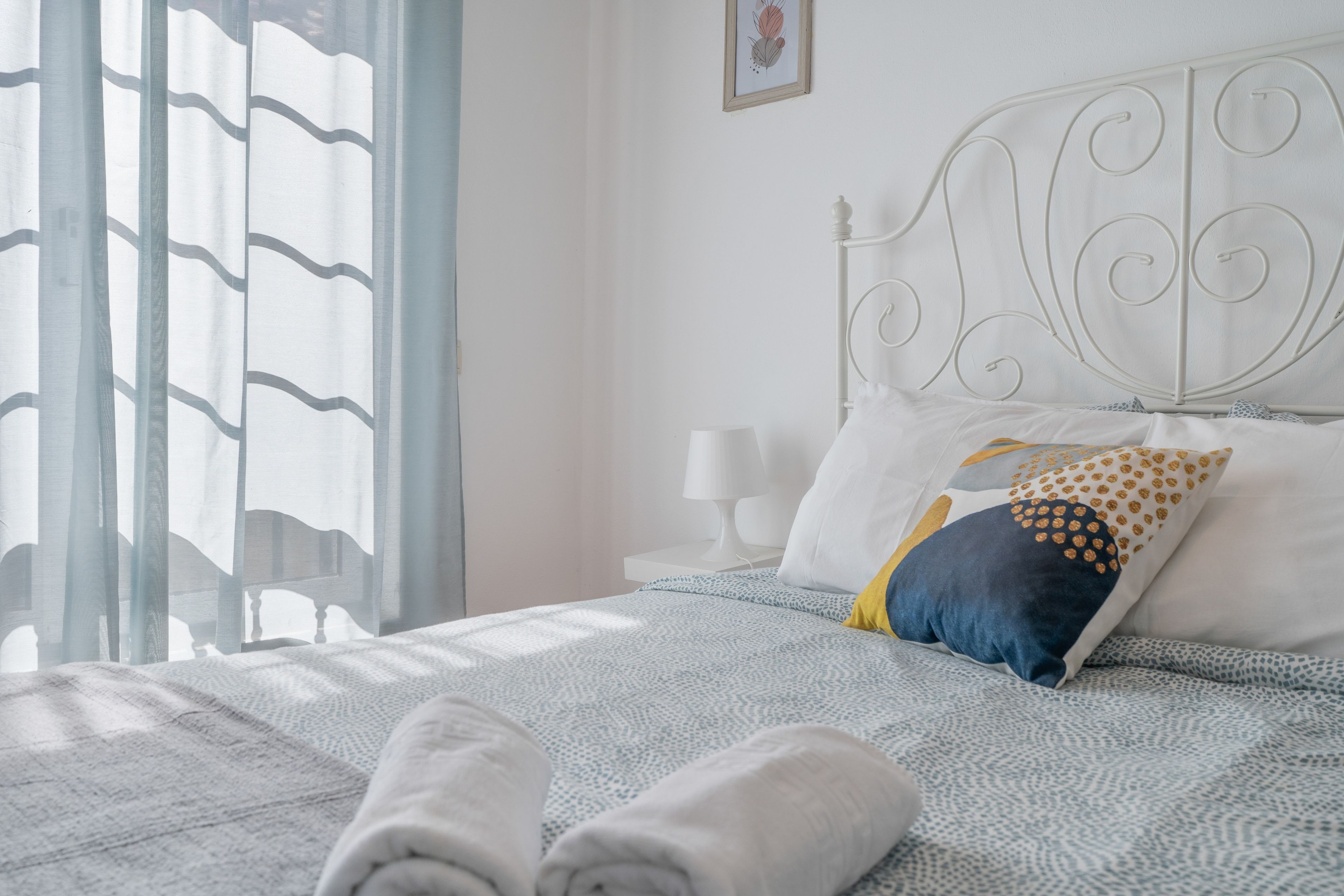 A neatly made bed with a patterned bedspread, a pillow with a geometric design, and a pair of folded towels on the bed.