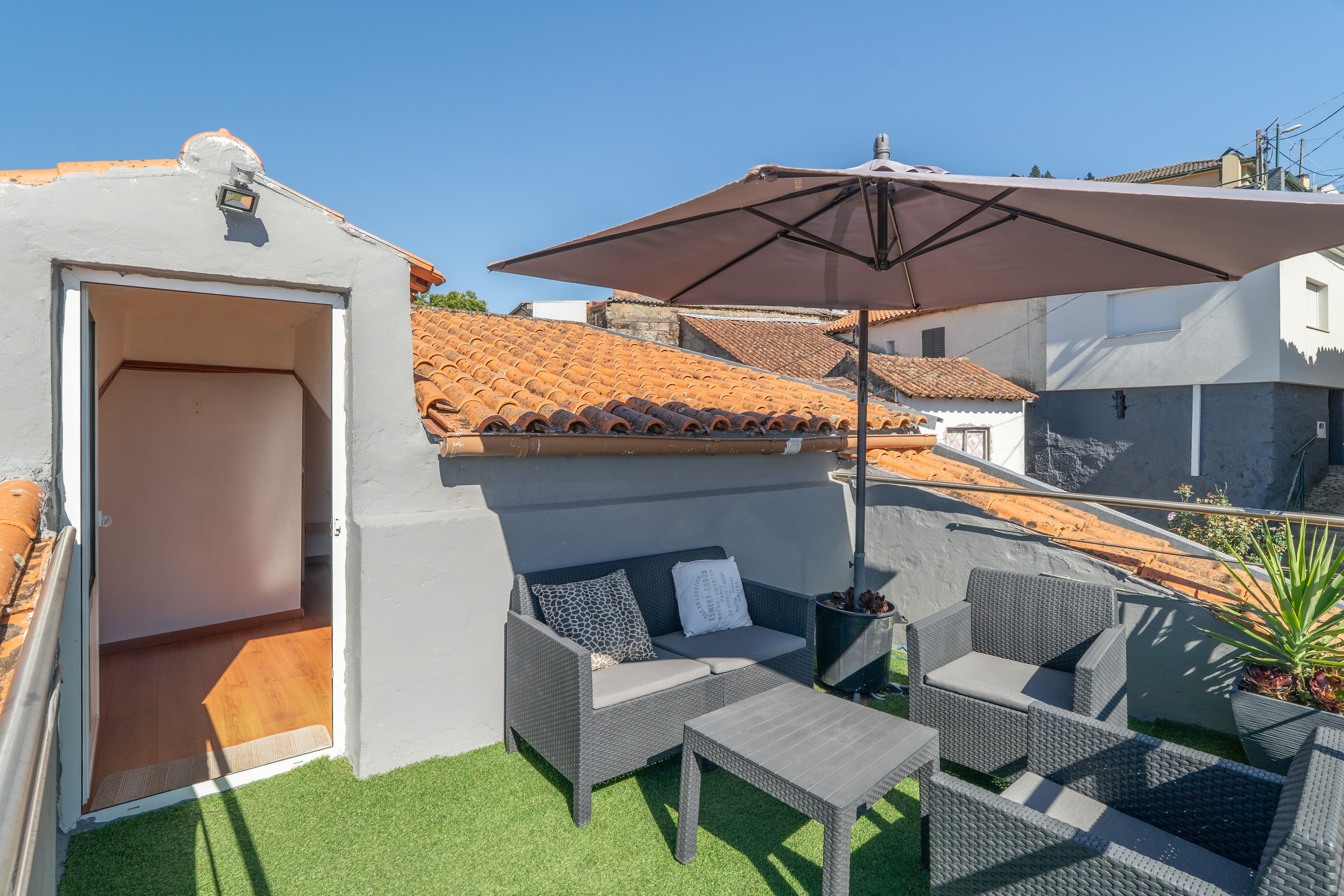 An outdoor seating area with wicker furniture and a large umbrella, set against a backdrop of terracotta-tiled roofs.