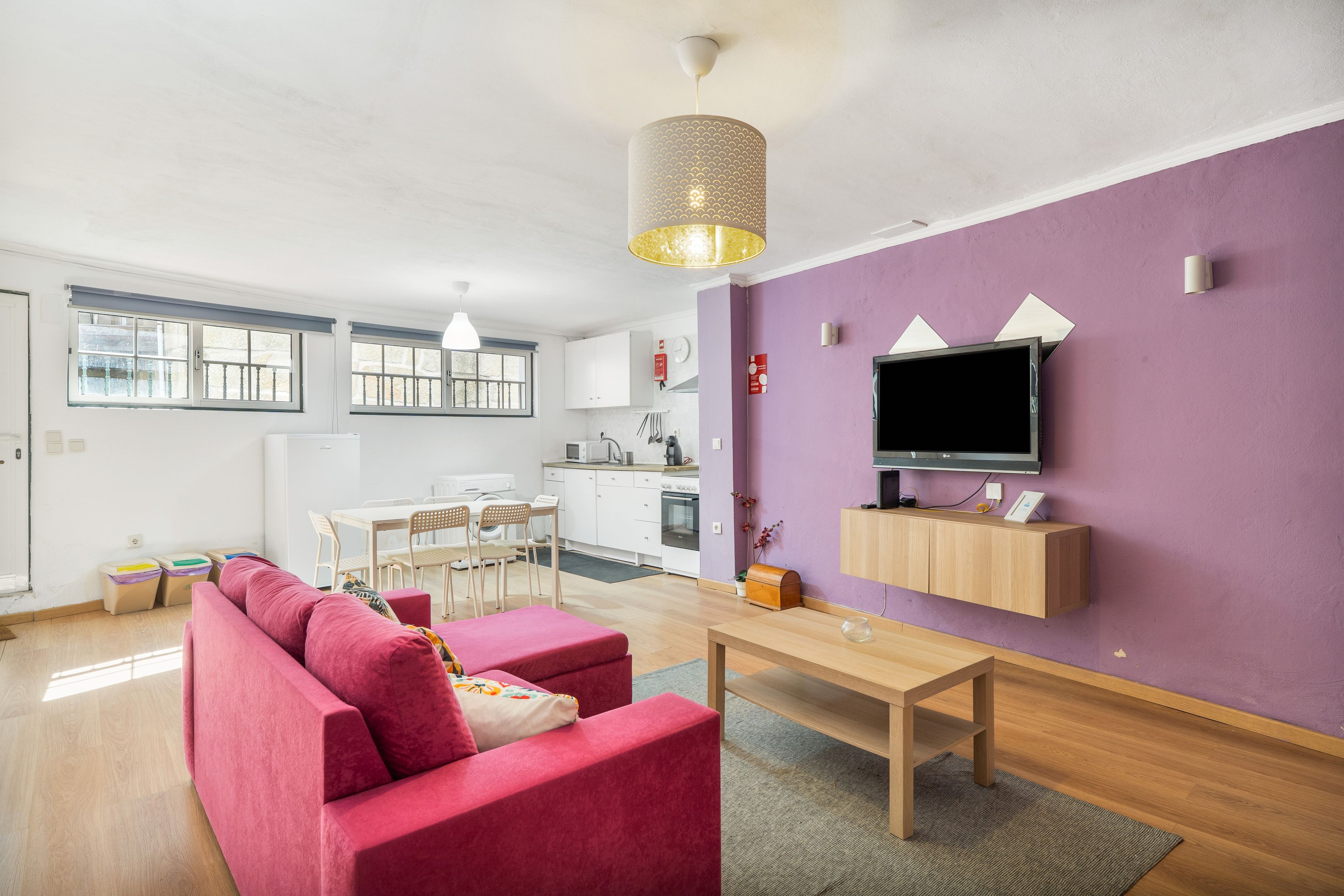 Uma sala de estar moderna com um sofá, uma mesa de jantar e uma TV fixada em uma parede roxa.