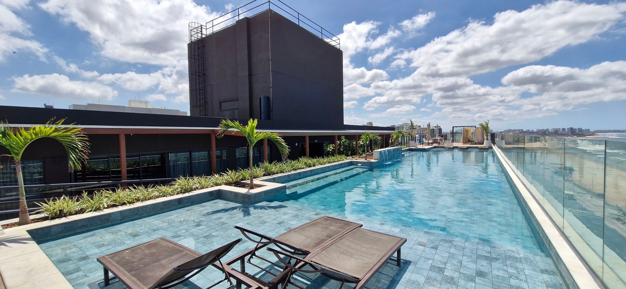 Uma piscina no terraço com água azul cristalina, rodeada por espreguiçadeiras e plantas em vasos.