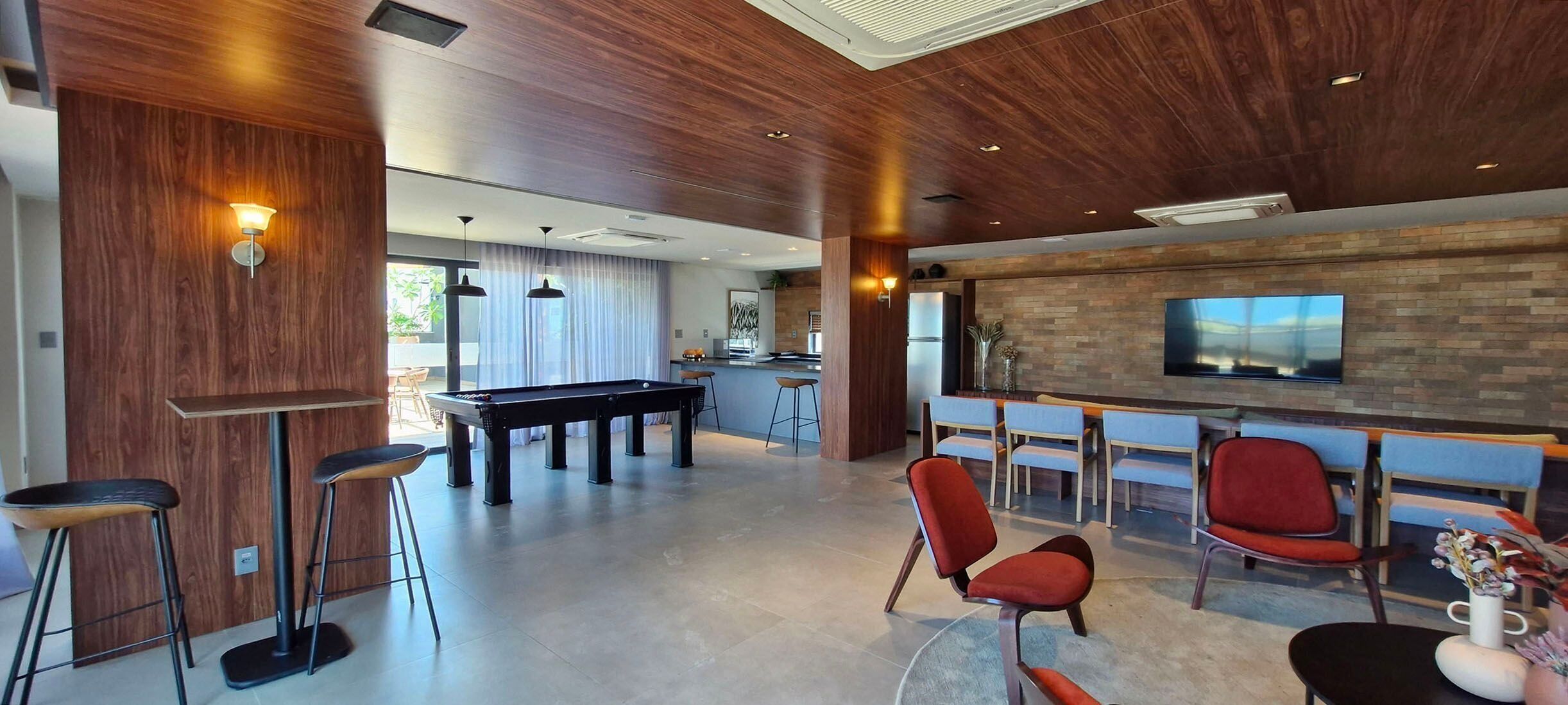 Un salon moderne avec une table de billard, des fauteuils rouges et un téléviseur fixé à un mur en briques.