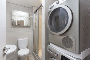 Et lille badeværelse med toilet, håndvask og en indbygget vaskemaskine.