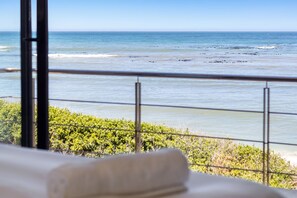 A view from a balcony overlooking a beach with waves, a clear sky, and a metal railing. - Hangklip Villa - Four Bedroom House, Sleeps 8 (Pringle Bay)
