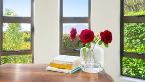 A wooden table with books and a vase of red roses by a window with a view of greenery and mountains. - Riebeek-Kasteel Villa (Riebeek-Kasteel)