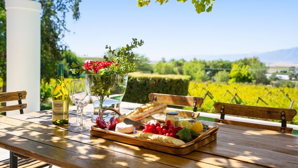 A wooden table with a bottle of wine, glasses, a fruit platter, and a baguette. - Riebeek-Kasteel Villa (Riebeek-Kasteel)