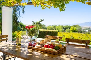 A wooden table with a bottle of wine, glasses, a fruit platter, and a baguette.