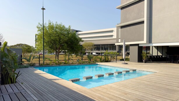 Ein modernes Gebäude mit Swimmingpool, Holzdeck und Sitzgelegenheiten im Freien.