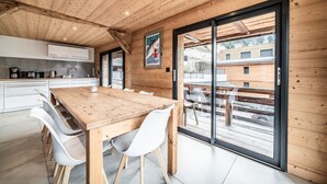 A modern kitchen with white cabinets, a wooden dining table, and a large sliding glass door leading to an outdoor area. - Martonne - Le Haut Apartment: Mountain View, Private Terrace & Wi-Fi (Châtel)