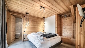 A wooden cabin bedroom with a bed, a hanging light fixture, and a white wall. - Martonne - Le Haut Apartment: Mountain View, Private Terrace & Wi-Fi (Châtel)