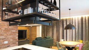 Une cuisine moderne dotée d’une cuisinière intégrée, un coin repas avec une table ronde et des chaises colorées, et un salon avec un canapé vert.