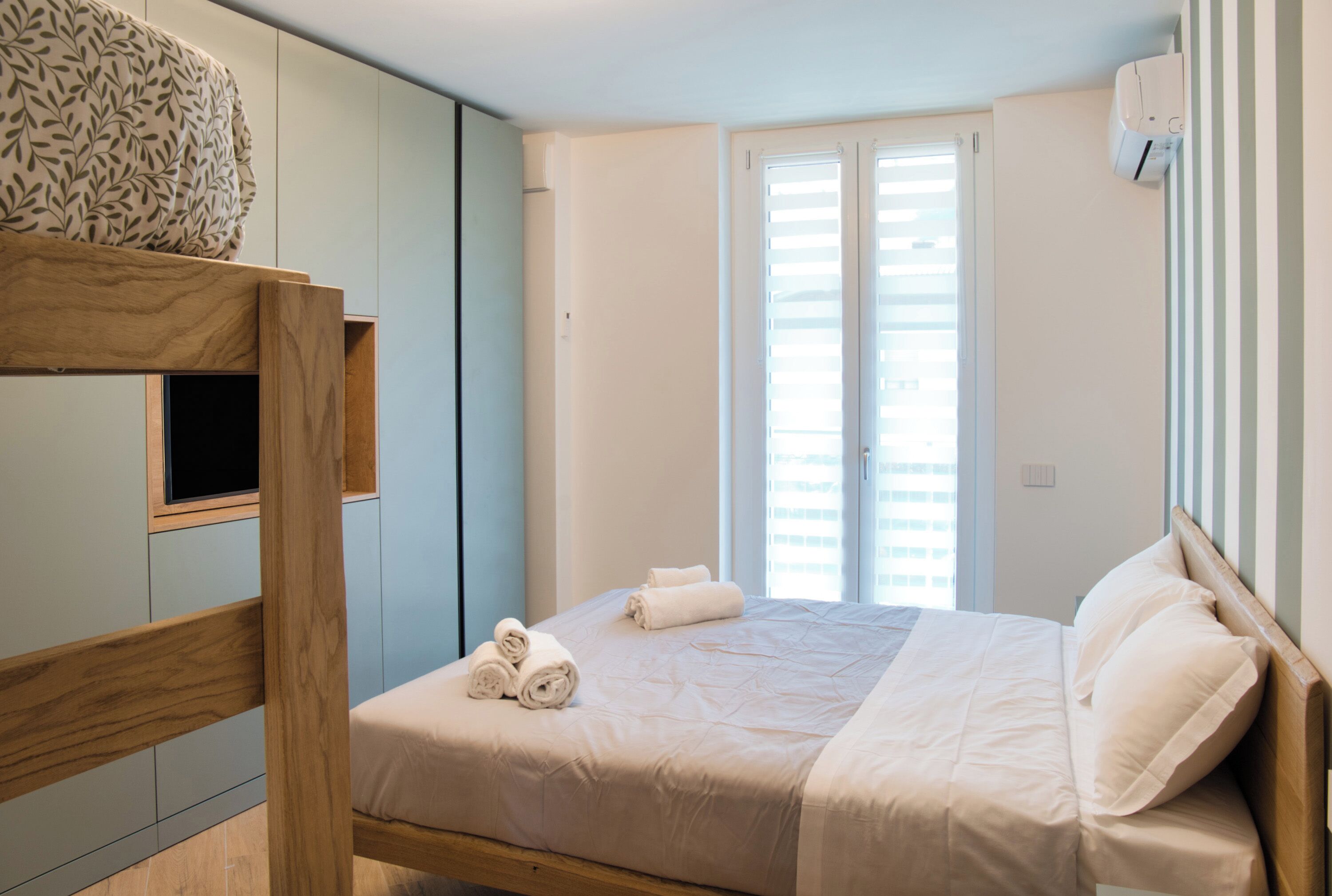 A bedroom with a bed, a wooden headboard, a window with blinds, and a wall-mounted air conditioner.