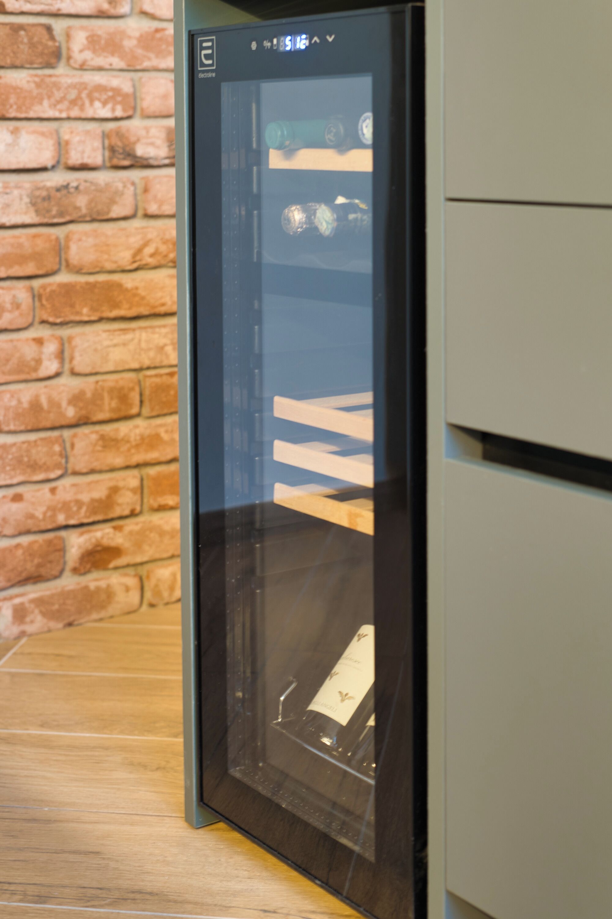 Un electrodoméstico con puerta de cristal, probablemente un refrigerador, en una cocina con pared de ladrillo.