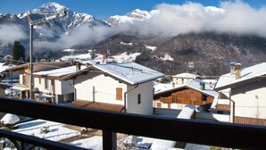 A residential area with snow-covered roofs and houses, a crane, and mountains in the background. - Achillea - trilocale in verde con vista montagne (Cremeno)