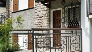 A stone building with a balcony, wooden shutters, and a wrought iron railing. - Achillea - trilocale in verde con vista montagne (Cremeno)