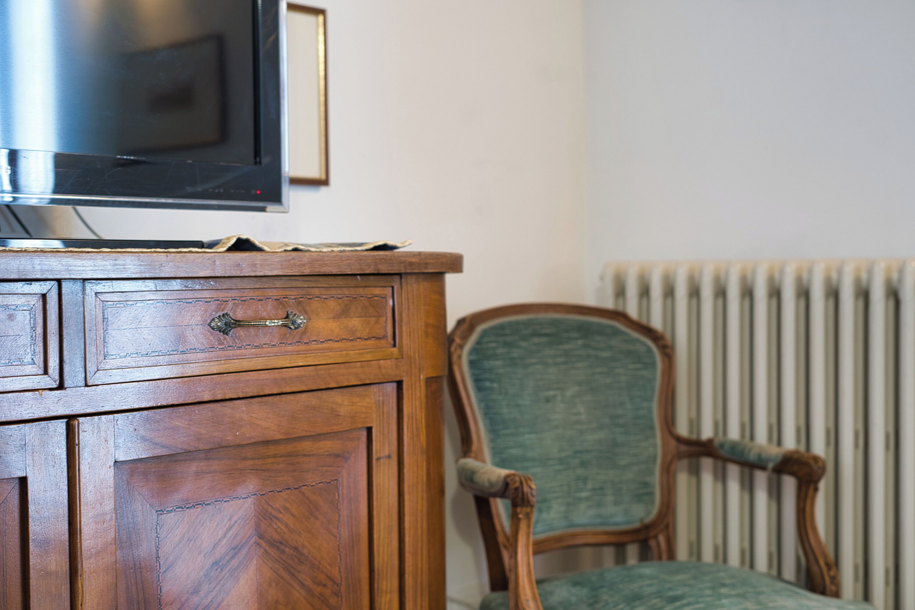 A wooden cabinet with a television on top, a green upholstered chair, and a radiator in the background.