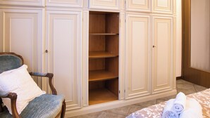 A room with a wooden chair, a bed with rolled towels, and a large wardrobe with multiple shelves. - Achillea - trilocale in verde con vista montagne (Cremeno)