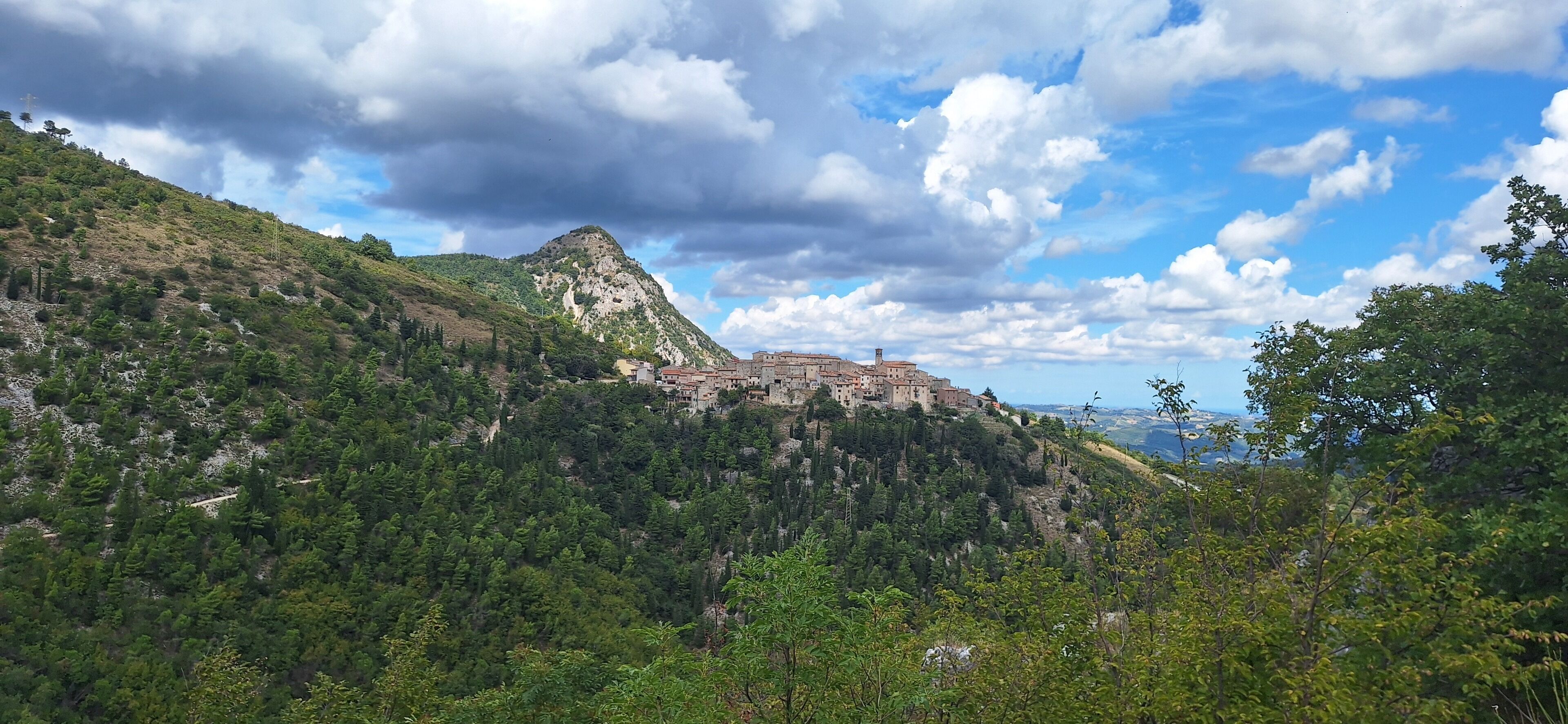 Eine gebirgige Landschaft mit einer historischen Stadt, die sich an einem Hügel schmiegt, umgeben von dichten Wäldern.