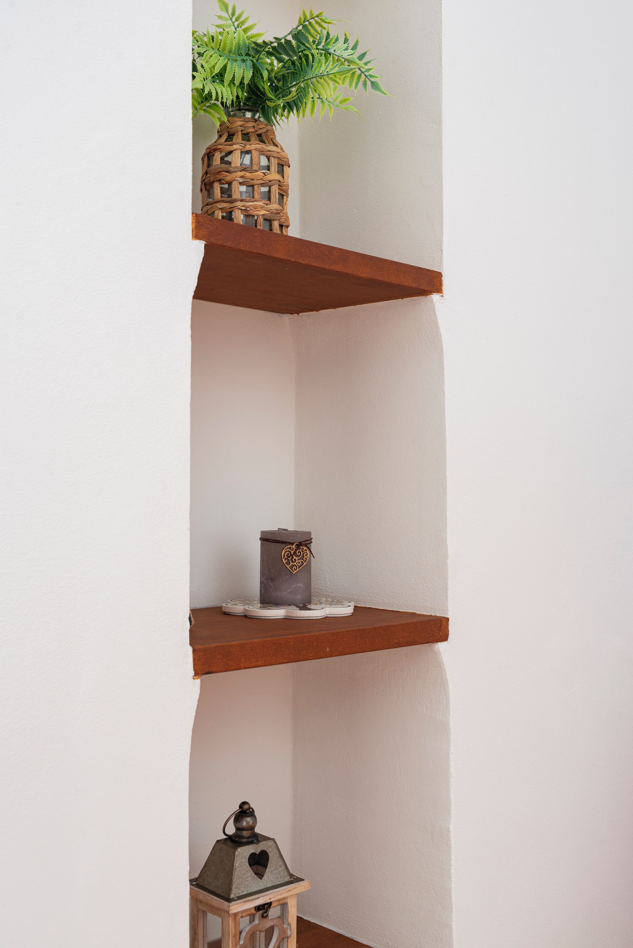 A corner shelf with a woven basket containing a plant, a heart-shaped box, and a lantern.