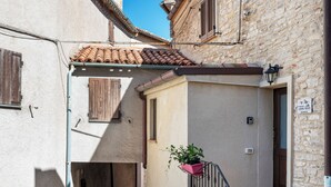Une ruelle étroite bordée d’immeubles en pierre, avec un clocher visible et un escalier menant à une porte.