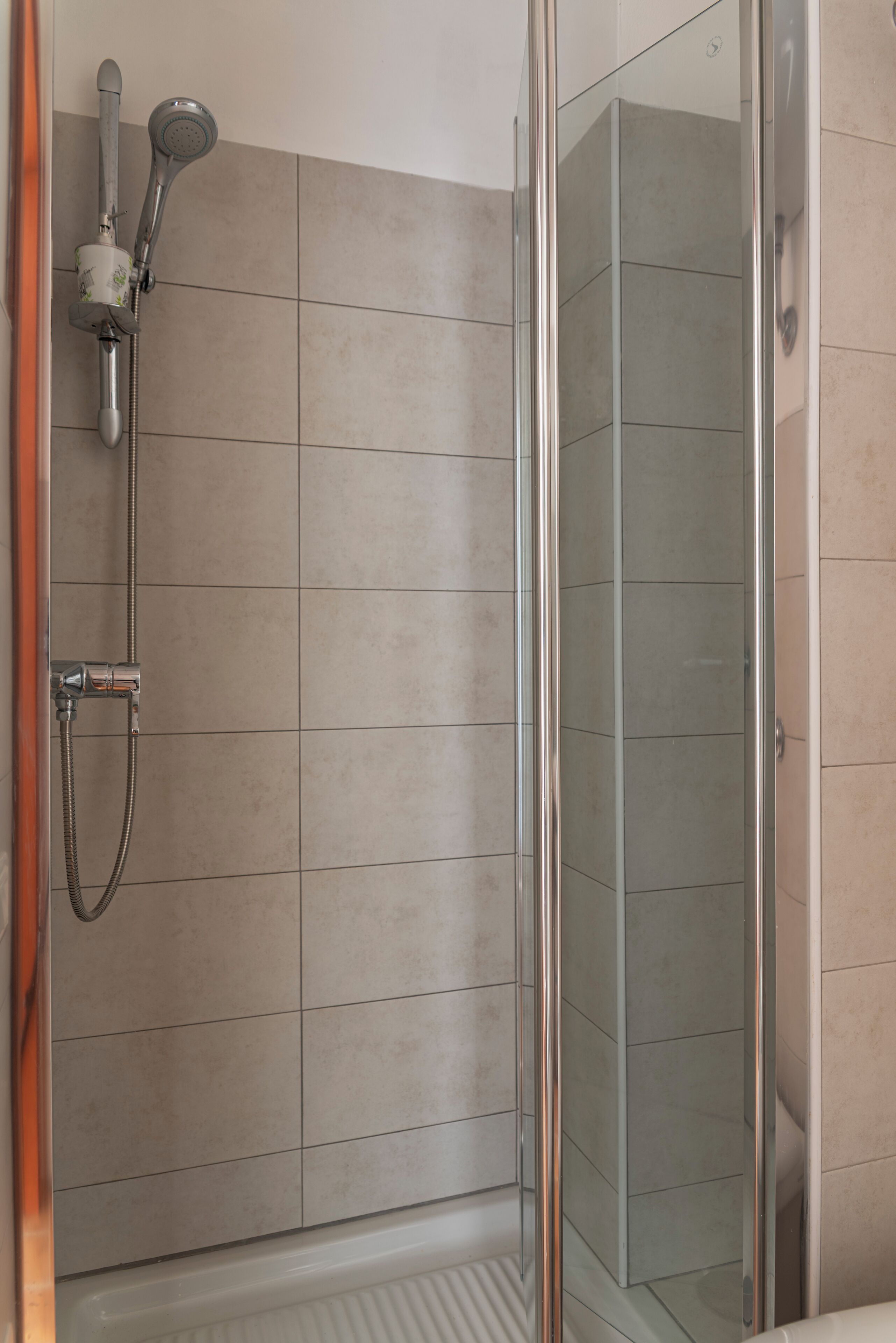 Une douche fermée par des parois en verre, dotée d’un pommeau de douche à main et d’un robinet mural.