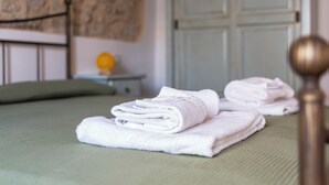 Un lit bien fait, avec des serviettes blanches pliées, un cadre de lit en métal, un oreiller vert et un mur orné d’un motif texturé.