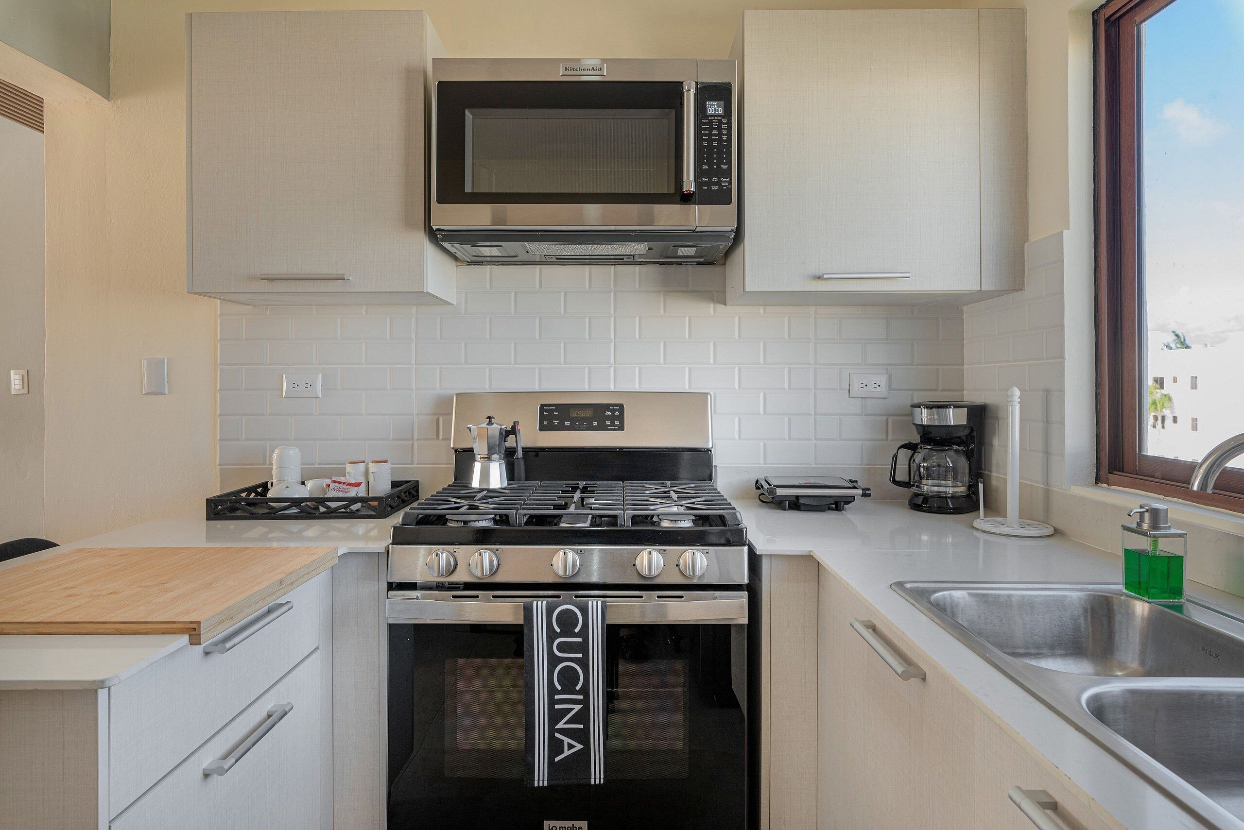 A modern kitchen with a built-in microwave, stove, and oven, featuring a 'Cucina' branded towel.