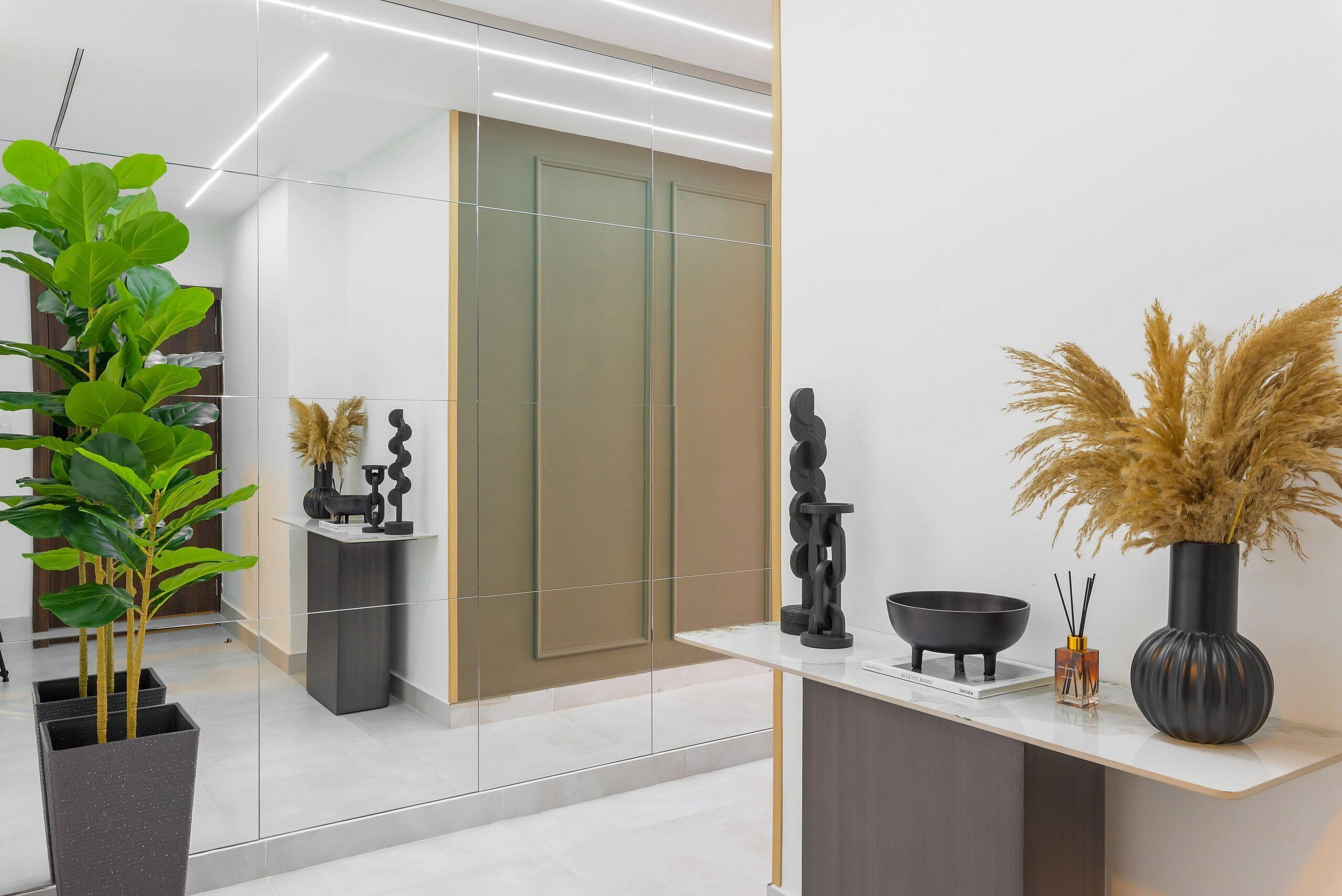A modern interior with a reflective wall, a potted plant, a black sculpture, and a vase with pampas grass.