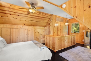 A wooden cabin interior with a bed, a ceiling fan, a window, and a wooden bench. - Secluded 3-bedroom log cabin in  Lake Arrowhead on one acre. (Lake Arrowhead)
